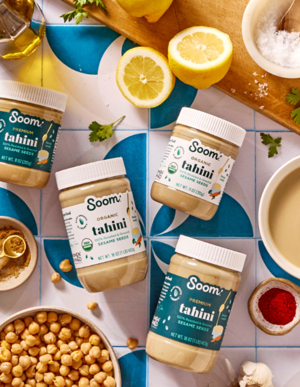 Soom tahini jars on a colorful tile background with lemons and chickpeas.